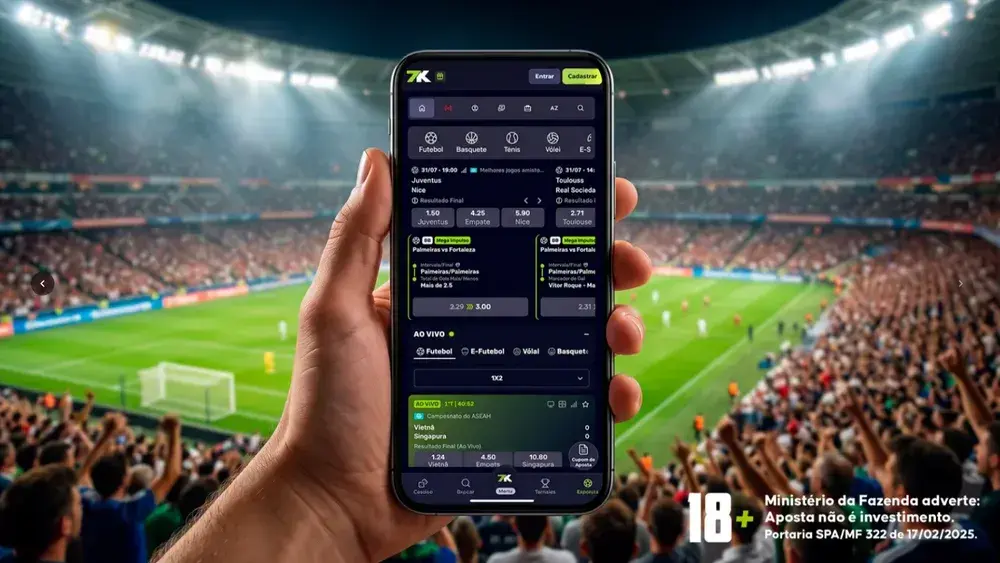 Mão segurando celular com os mercados de apostas da 7K Bet abertos, ao fundo um estádio de futebol lotado
