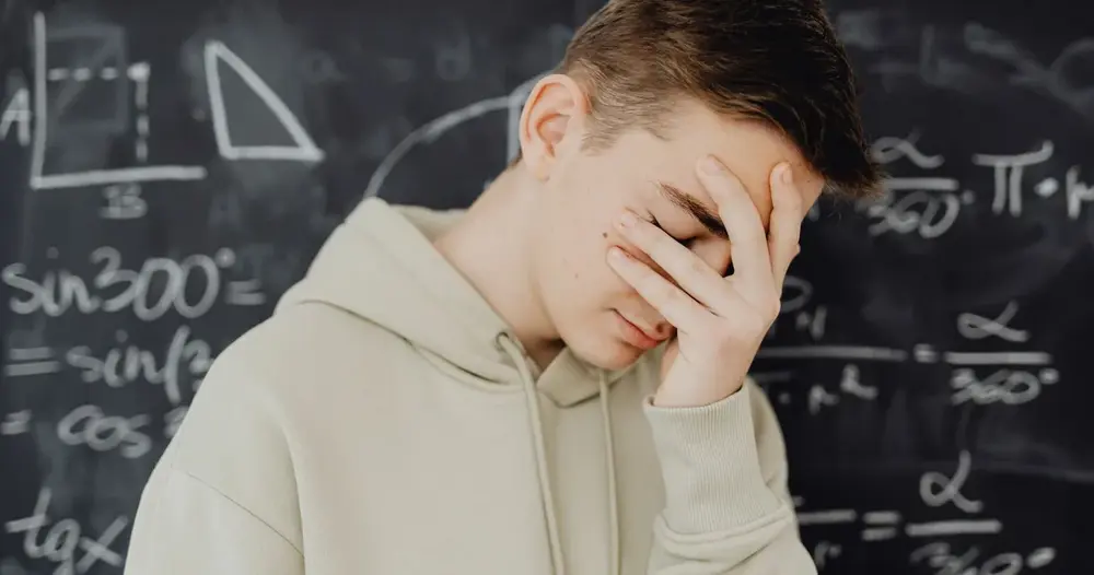 Jovem sobrecarregado por cálculos matemáticos em um quadro negro em ambiente de sala de aula.